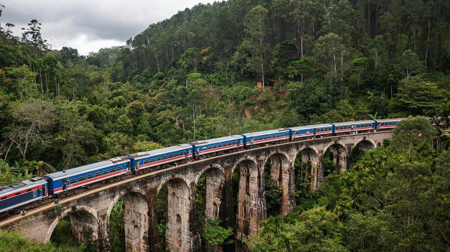 A blue train crossing the Nine Arch Bridge above the jungle in Ella, Sri Lanka